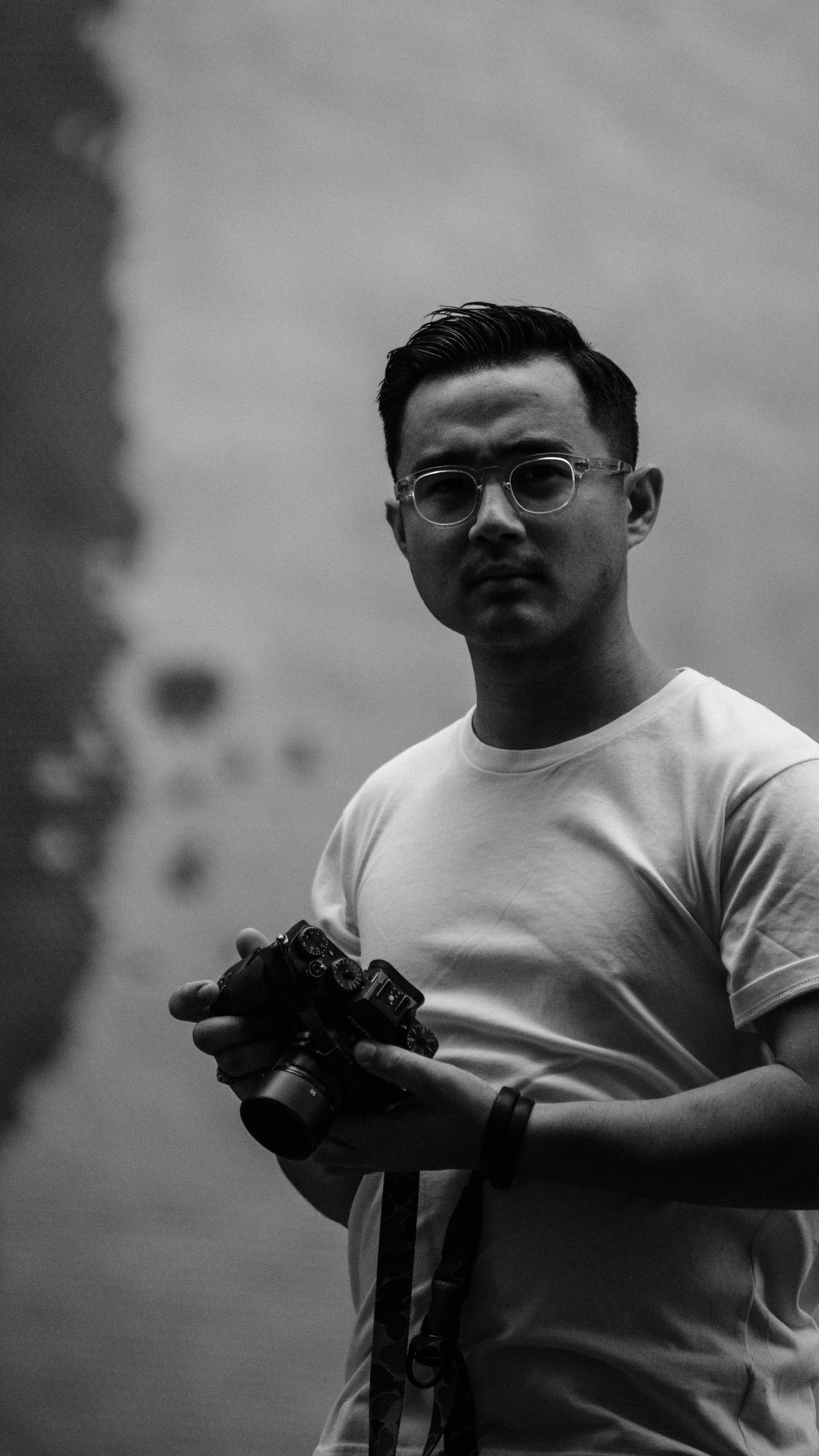 Grayscale Photo of Man Wearing Crew-neck T-shirt Standing While Holding Dslr Camera